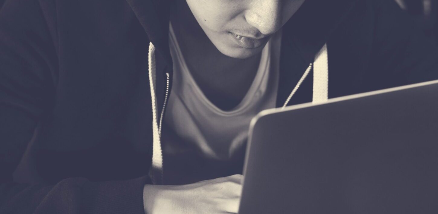 Young person in a hoodie looking at a laptop screen, highlighting online sextortion awareness