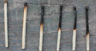 Six matches lined up on a wooden surface, each progressively more burned from left to right.