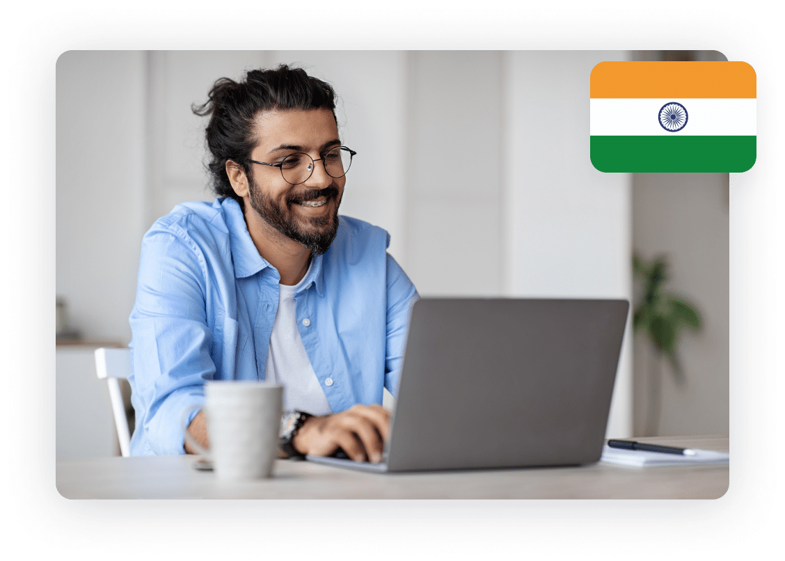 Man smiling and working on a laptop with an Indian flag, representing compliance and regulation