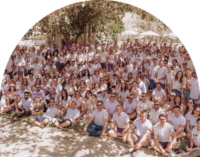 Large group of people in white shirts posing outdoors under a large tree.